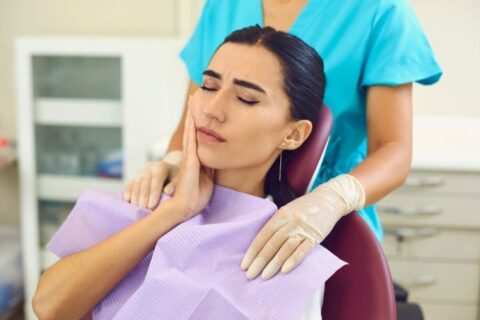 Woman at dentist holding her cheek in pain due to sensitive teeth after whitening treatment.